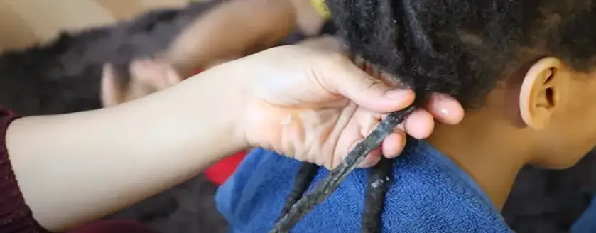 A mother conditioning her son's hair as she prepares to comb out his dreadlocks | Source: YouTube/ Kiesha Arielle